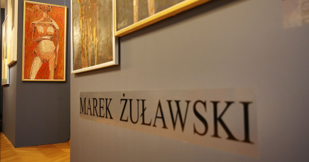 Zbliżenie na ścianę, na której pod obrazami umieszczono nazwisko autora: Marek Żuławski.
