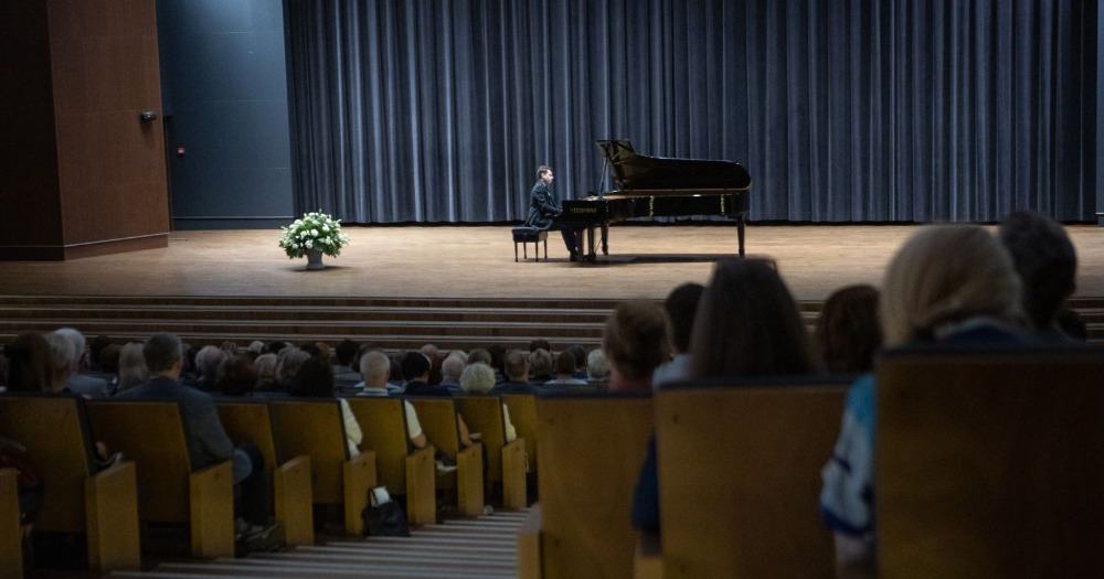 Scena, na której stoi fortepian, przy którym siedzi pianista. Widoczna jest także widownia: fotele oraz uczestnicy koncertu.
