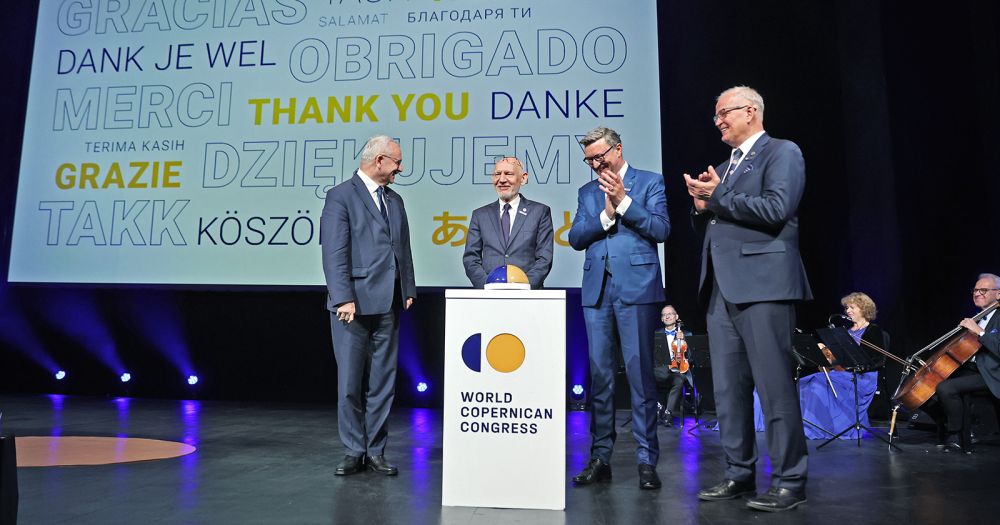 Czterech mężczyzn stoi na scenie przed specjalnym przyciskiem nawiązującym do logotypu Światowego Kongresu Kopernikańskiego. Wciśnięcie przycisku ma być symbolem rozpoczęcia Kongresu