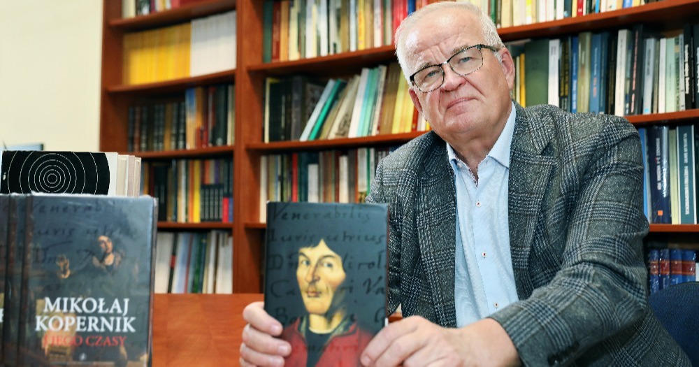 Mężczyzna w dojrzałym wieku pozujący do zdjęcia z książką pt. "Mikołaj Kopernik", której jest autorem