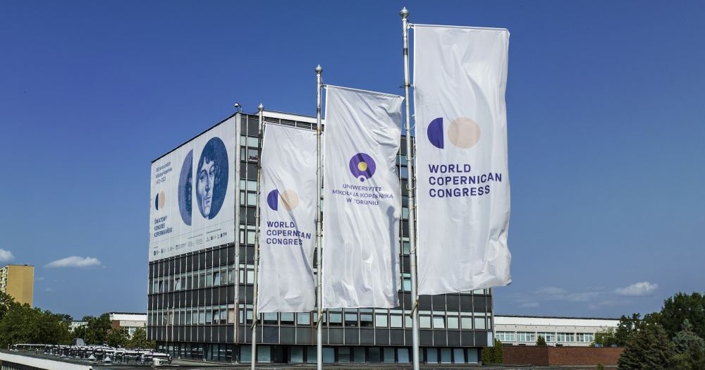 Rektorat UMK z banerem promującym Światowy Kongres Kopernikański i 3 flagi z symbolami Kongresu.